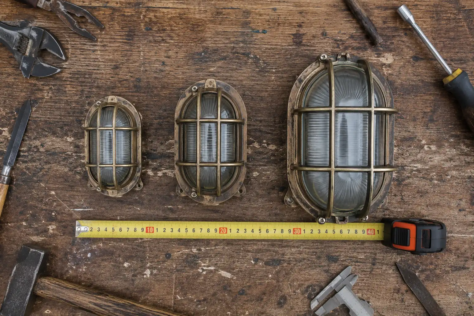 Three reclaimed bulkhead light sizes compared with a tape measure on a workbench
