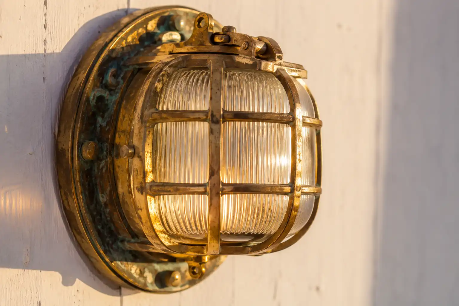 Caged brass bulkhead light with prismatic glass mounted on a white coastal wall