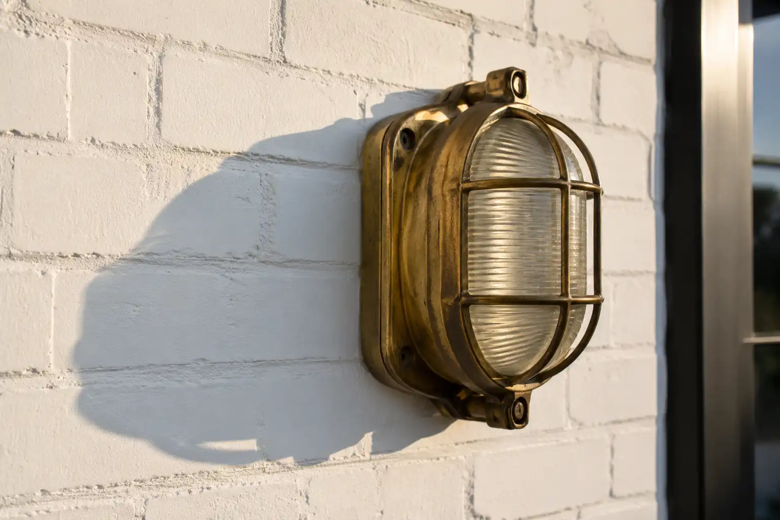Side view of a caged brass bulkhead light showing projection from a painted brick wall