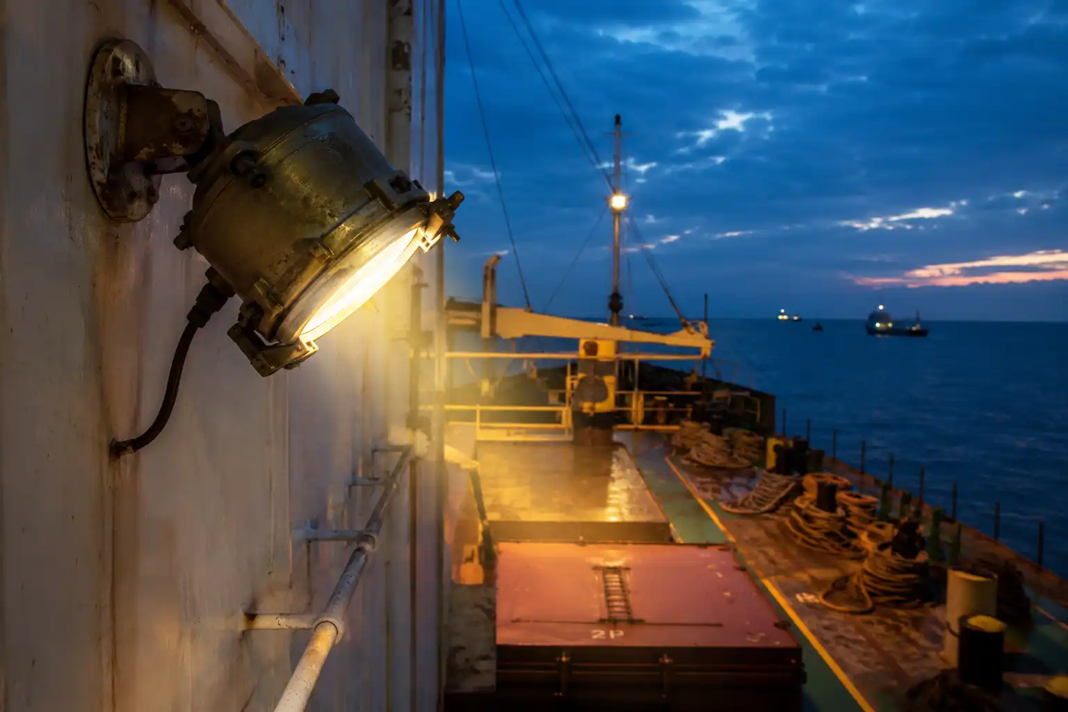 Brass ship deck light lighting the working deck of a cargo ship at dusk