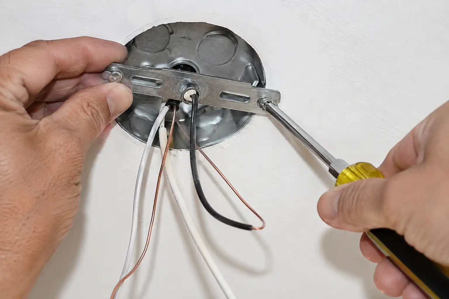 Worker mounting a crossbar strap to a ceiling junction box during a pendant light installation