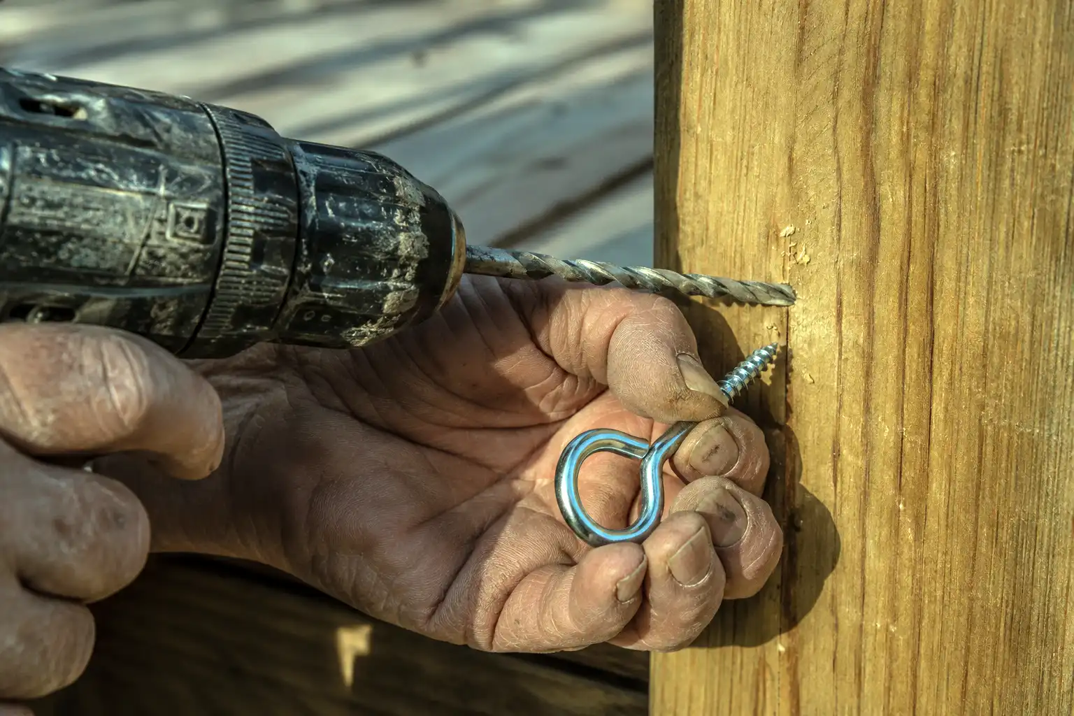 Pre drilling a pilot hole for a stainless screw eye before stringing lights on a wooden deck post